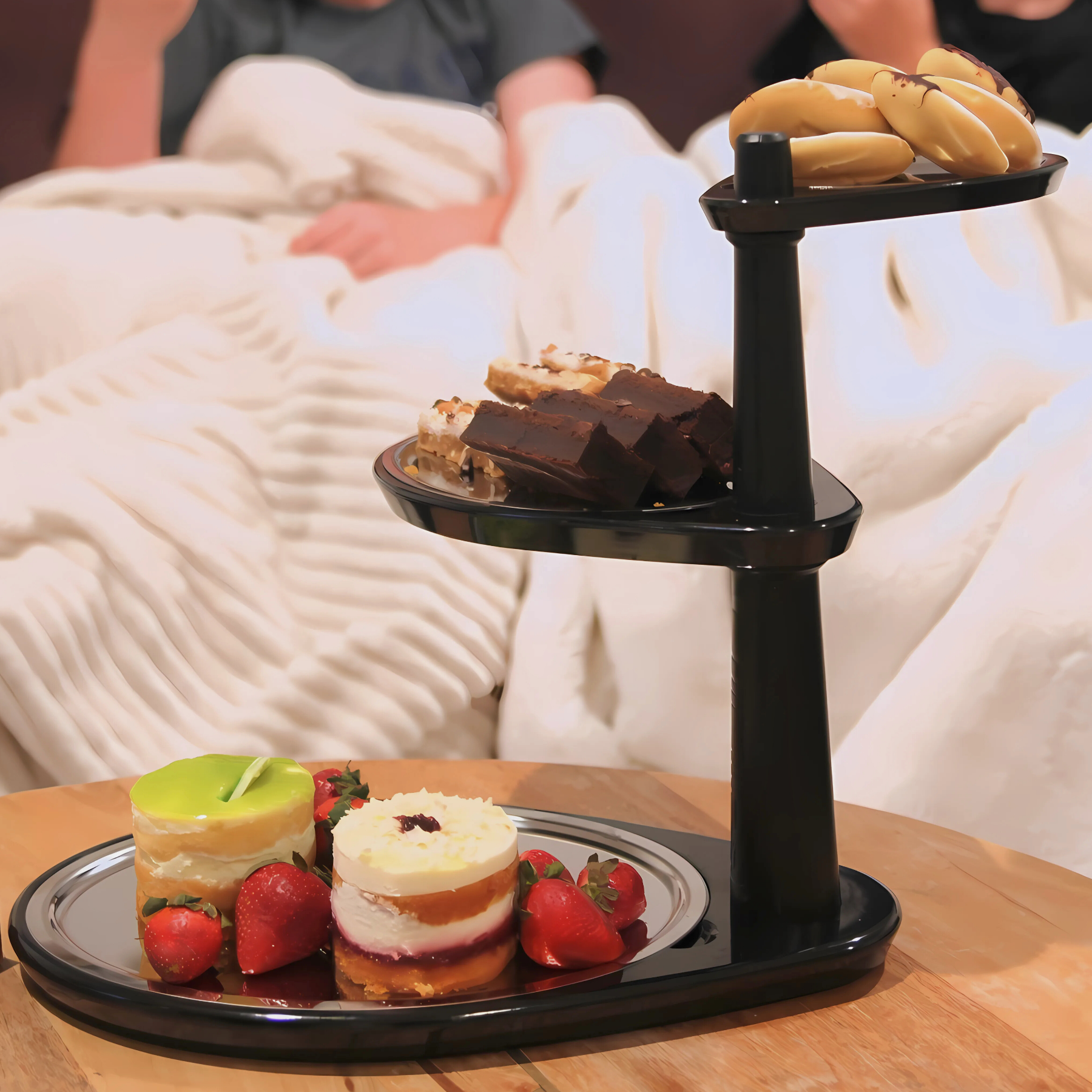 Three-tiered black serving tray with desserts on a wooden table.
